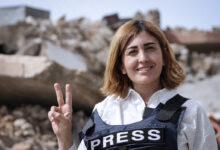 Lübnanlı gazeteci Amal Khalil üzerinde PRESS yazılı çelik yelekle enkaz önünde zafer işareti yaparken.