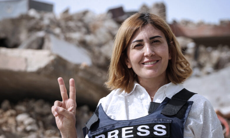 Lübnanlı gazeteci Amal Khalil üzerinde PRESS yazılı çelik yelekle enkaz önünde zafer işareti yaparken.
