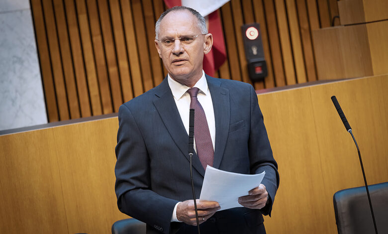 Avusturya Ulusal Meclisi (Nationalrat) oturumunda konuşma yapan bir milletvekili, arka planda meclis üyeleri ve Avusturya bayrağı.