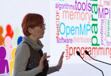 AI Factory Austria Öğrenme Merkezi Başkanı Claudia Blaas-Schenner, arkasında yapay zeka ve programlama terimlerinden oluşan bir kelime bulutu panosuyla sunum yaparken.