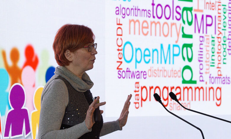 AI Factory Austria Öğrenme Merkezi Başkanı Claudia Blaas-Schenner, arkasında yapay zeka ve programlama terimlerinden oluşan bir kelime bulutu panosuyla sunum yaparken.