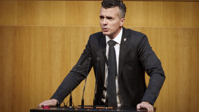 FPÖ Güvenlik Sözcüsü Gernot Darmann, Avusturya Parlamentosu kürsüsünde konuşma yaparken kararlı bir ifadeyle kürsüye tutunuyor.