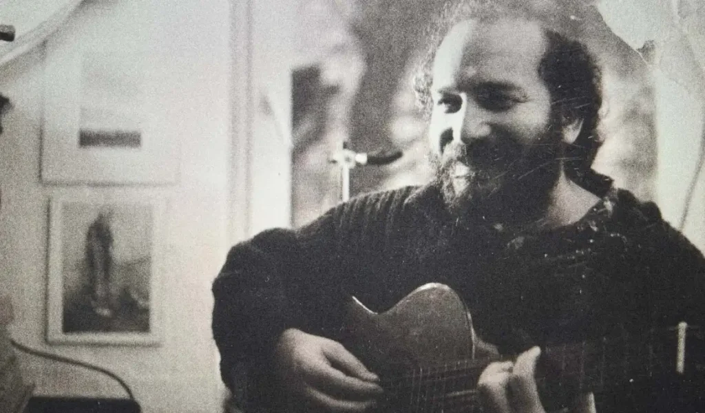 Usta sanatçı Fuat Saka elinde gitarıyla siyah beyaz bir arşiv fotoğrafında şarkı söylerken.