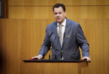 FPÖ Sağlık Sözcüsü Gerhard Kaniak, Avusturya Parlamentosu kürsüsünde takım elbisesiyle mikrofonlar önünde konuşma yapıyor.