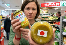 Avusturya SPAR marketinde HiPP bebek maması kavanozunun altındaki kırmızı daireli uyarı işaretini gösteren bir kadın.