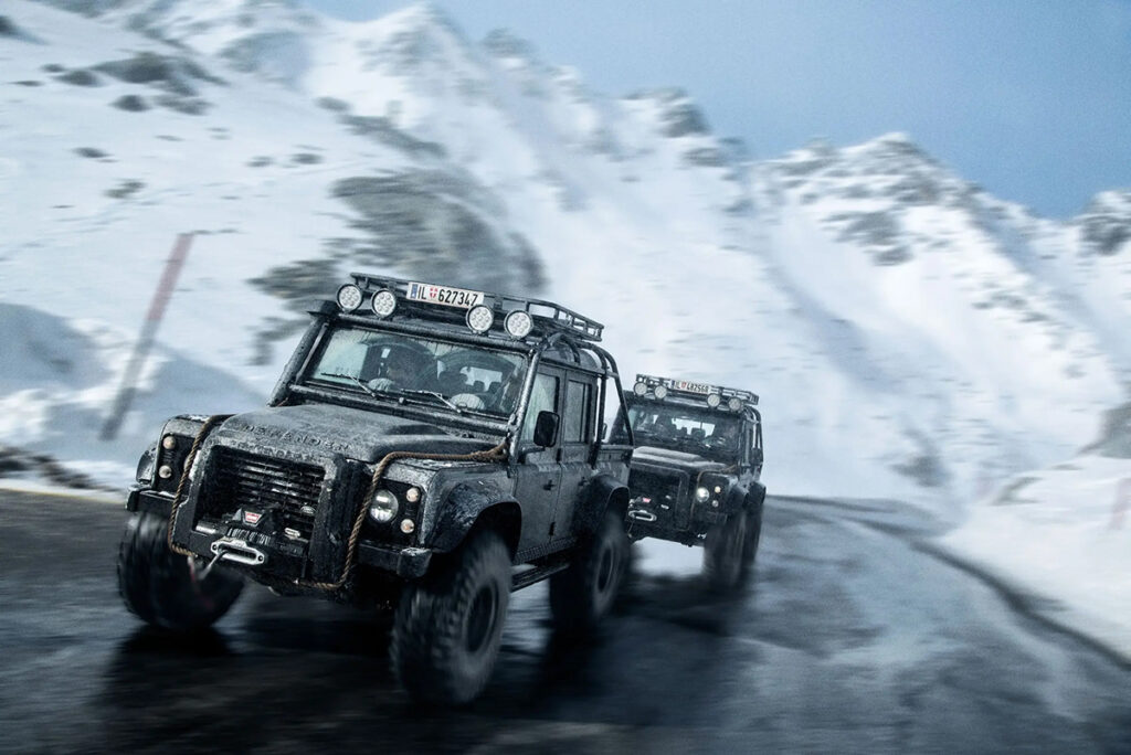 Karlı yolda hızla giden siyah Land Rover Defender araçlar - James Bond Spectre sahnesi.