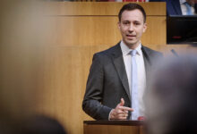 ÖVP Genel Sekreteri Nico Marchetti, meclis kürsüsünde ceketli ve kravatlı bir şekilde, işaret parmağıyla vurgu yaparak konuşma yapıyor.