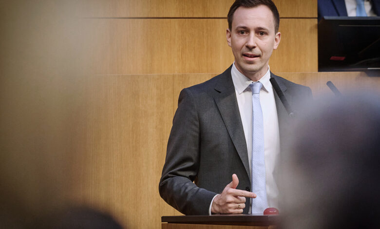 ÖVP Genel Sekreteri Nico Marchetti, meclis kürsüsünde ceketli ve kravatlı bir şekilde, işaret parmağıyla vurgu yaparak konuşma yapıyor.