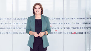 AK Başkanı Renate Anderl, Viyana İşçi Odası (AK) binasında, üzerinde işçi hakları vurgularının olduğu cam bir duvarın önünde profesyonel bir duruşla gülümsüyor.