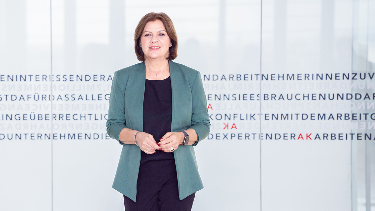 AK Başkanı Renate Anderl, Viyana İşçi Odası (AK) binasında, üzerinde işçi hakları vurgularının olduğu cam bir duvarın önünde profesyonel bir duruşla gülümsüyor.