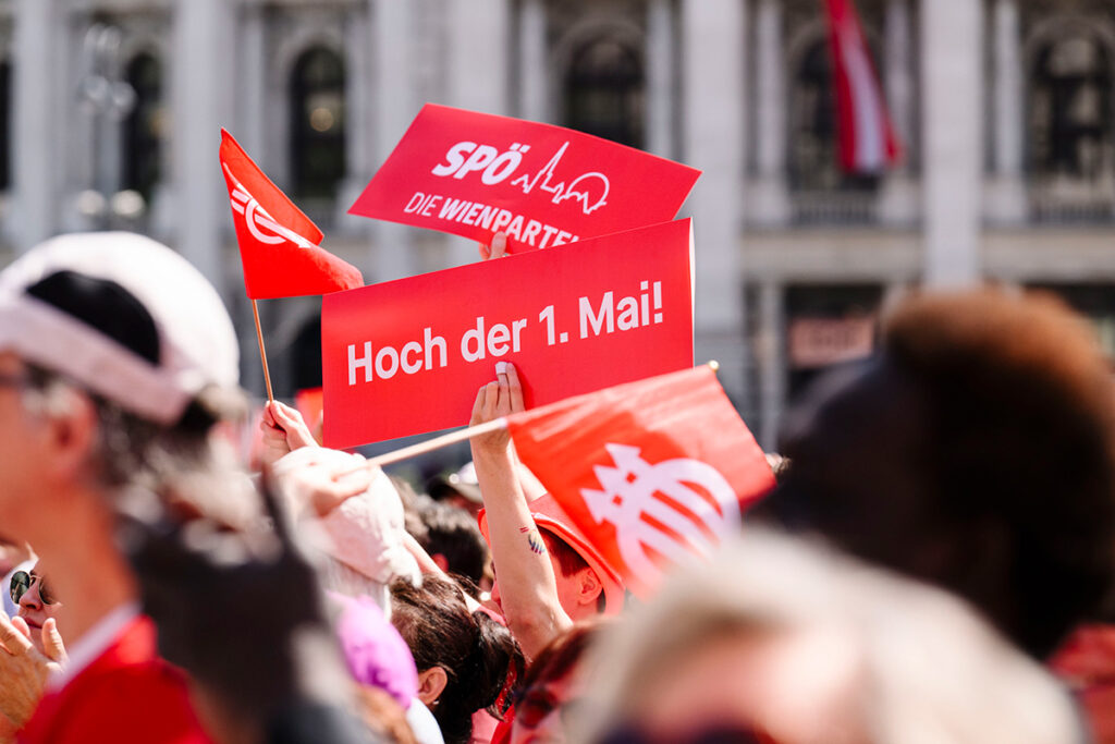 Viyana'da 1 Mayıs kutlamalarında ellerinde 'Hoch der 1. Mai!' yazılı tabelalar ve SPÖ bayrakları tutan kalabalık bir grup.