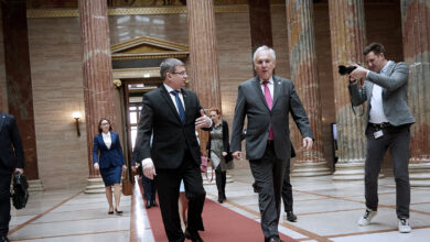 Avusturya Ulusal Meclis Başkanı Walter Rosenkranz ve Moldova Parlamento Başkanı Igor Grosu, Viyana'daki parlamento binasının görkemli sütunlu salonunda kırmızı halı üzerinde yürürken sohbet ediyor. Arka planda devasa mermer sütunlar ve bir fotoğrafçı görülüyor.