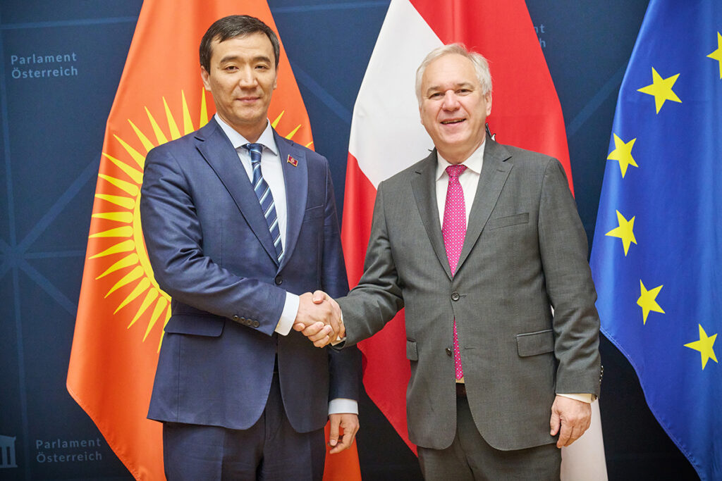 Walter Rosenkranz ve Kırgızistan Meclis Başkan Yardımcısı Mederbek Aliev, Avusturya ve Kırgızistan bayrakları önünde el sıkışıyor.