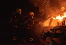 Avusturya'da gece karanlığında alevler içindeki yanan otomobili hortumla söndürmeye çalışan iki itfaiyeci temsili kaza fotoğrafı