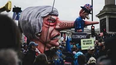 Londra'da Brexit karşıtı protestoda, burnu uzamış hicivli Theresa May ve mini Boris Johnson karikatürleri maketi. Üzerinde 'BREXIT' ve 'ECONOMY' yazılı bavul var.