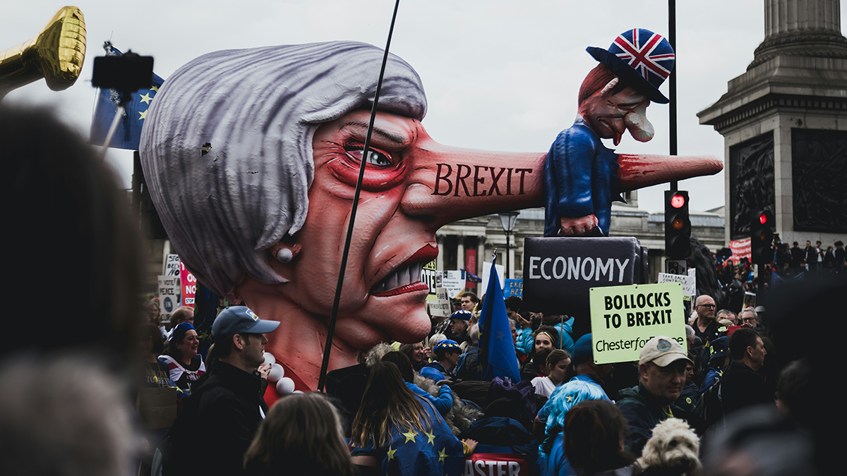 Londra'da Brexit karşıtı protestoda, burnu uzamış hicivli Theresa May ve mini Boris Johnson karikatürleri maketi. Üzerinde 'BREXIT' ve 'ECONOMY' yazılı bavul var.