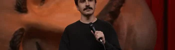 Komedyen Deniz Göktaş Ölü Deniz stand-up gösterisinde elinde mikrofonla sahnede konuşuyor