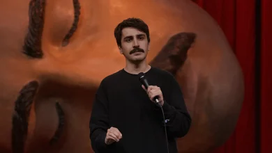 Komedyen Deniz Göktaş Ölü Deniz stand-up gösterisinde elinde mikrofonla sahnede konuşuyor