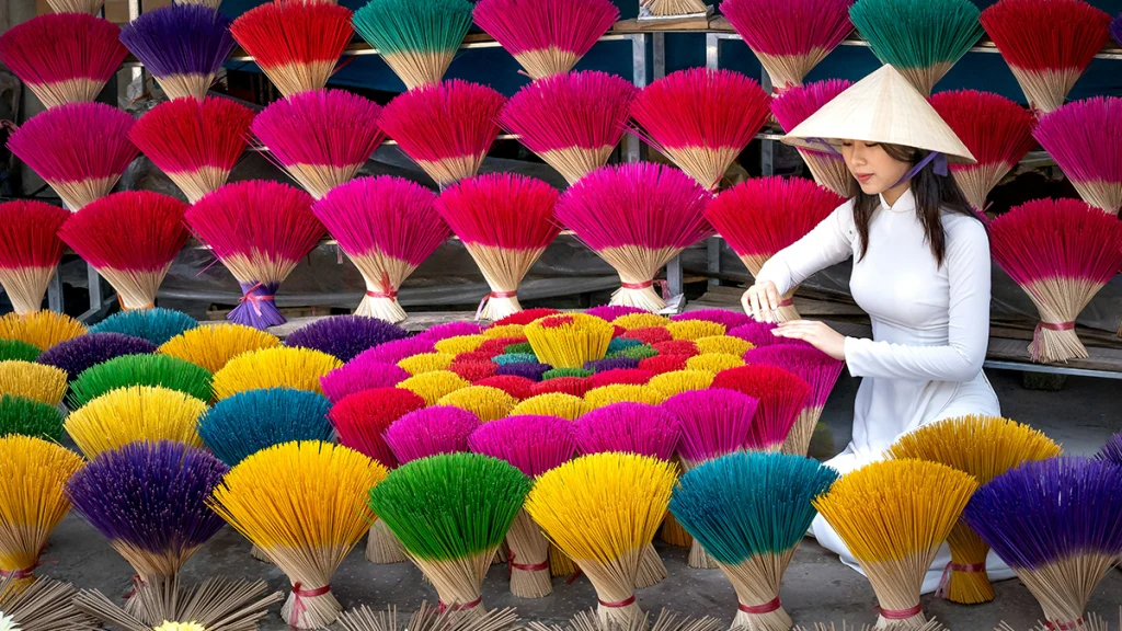 Vietnam'ın geleneksel beyaz Ao Dai elbisesini giymiş bir kadının Quảng Phú Cầu köyünde sarı, pembe, yeşil ve mavi tütsülerle dairesel sarmal oluşturması.