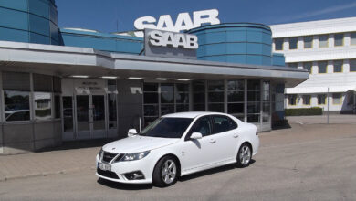 İsveç'teki tarihi Saab Trollhättan fabrikası binası önünde duran beyaz bir Saab 9-3 modeli