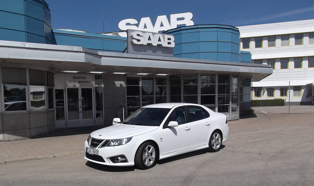 İsveç'teki tarihi Saab Trollhättan fabrikası binası önünde duran beyaz bir Saab 9-3 modeli