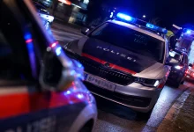 Avusturya'da gece vaktinde mavi ışıkları yanan bir polis arabası ve arka planda duran ambulans ile trafik kazası müdahale sahnesi.