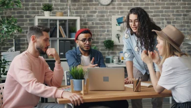 Modern bir ofis ortamında bilgisayar ekranı başında aktif şekilde iletişim kuran ve tartışan çok kültürlü genç profesyoneller grubu.