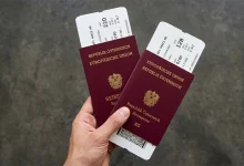 Bir kişinin elinde tuttuğu, içinde uçak biniş kartları bulunan iki adet koyu kırmızı renkli resmi Avusturya pasaportu.