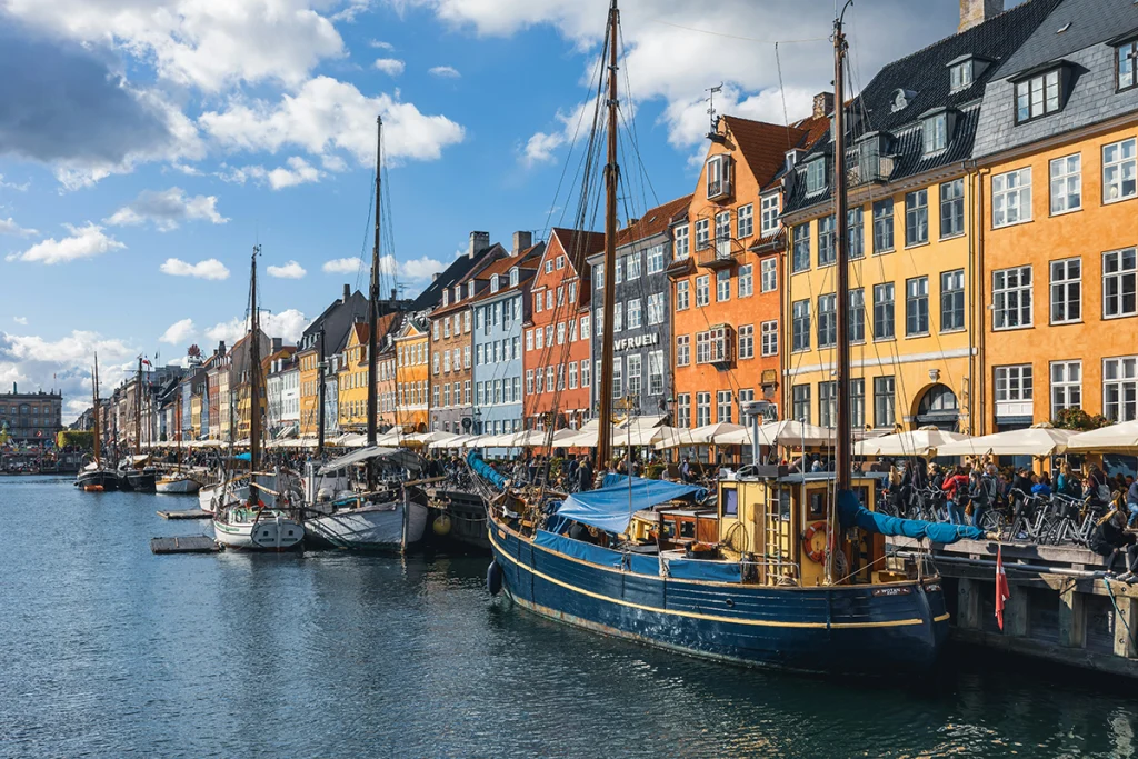 Kopenhag'daki Nyhavn Limanı'nda demirlenmiş tekneler ve arkada sıralanmış tarihi renkli evler.